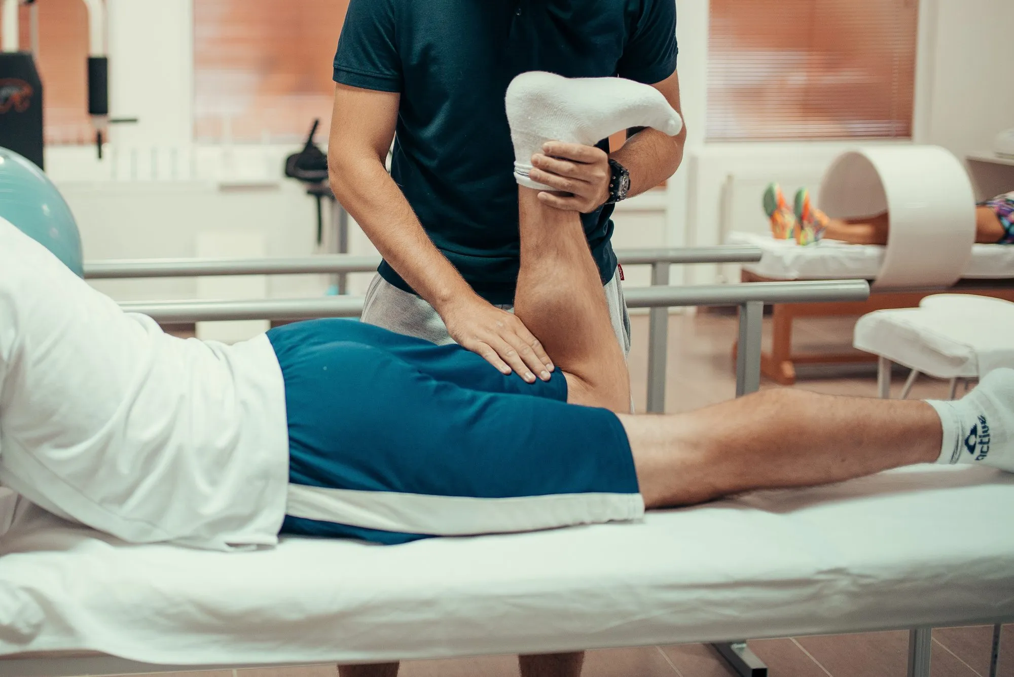 Ein Therapeut beugt das Bein eines Patienten, der auf der Behandlungsliege liegt