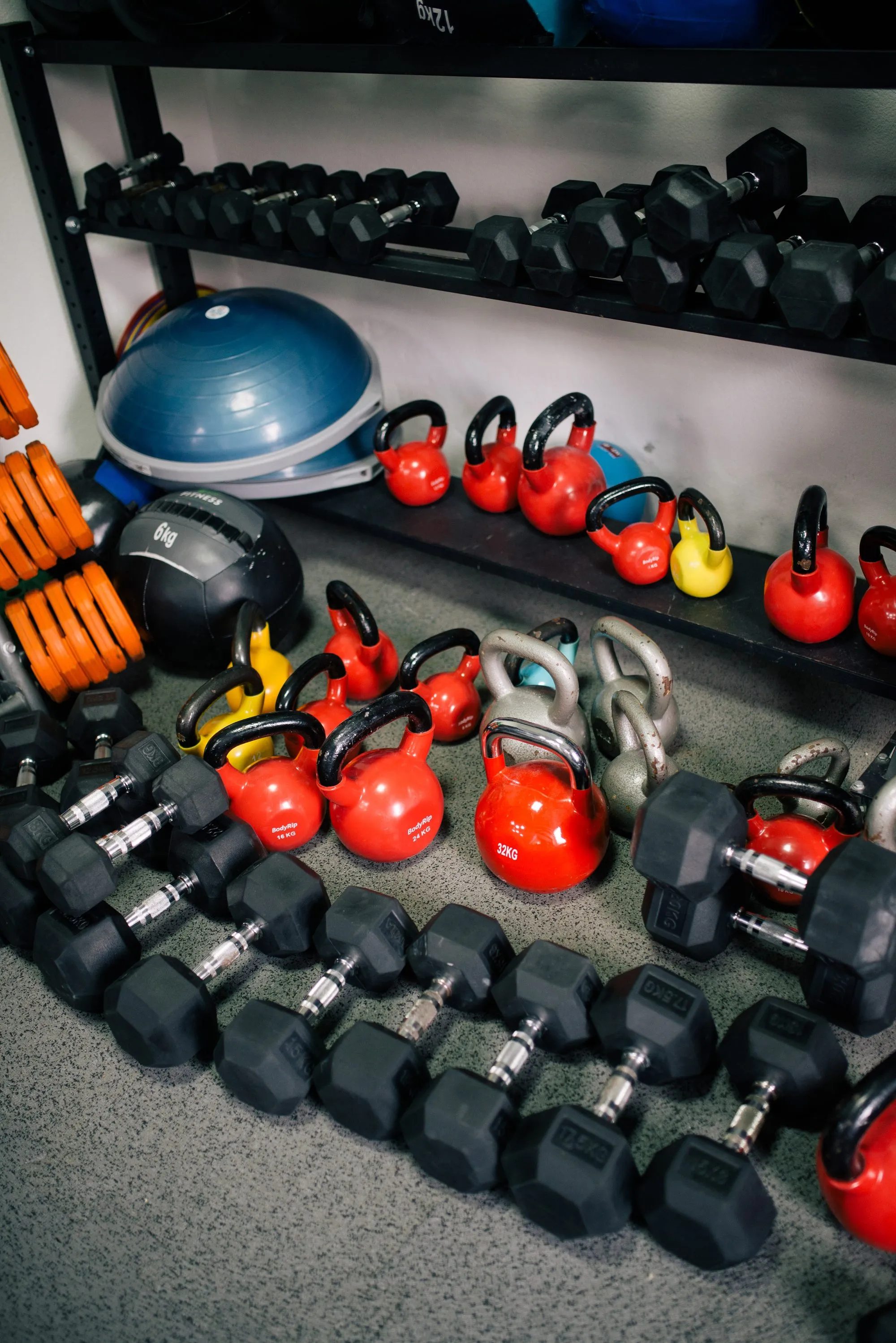 Bunte Kettlebells und schwarze Kurzhanteln im Regal und auf dem Boden