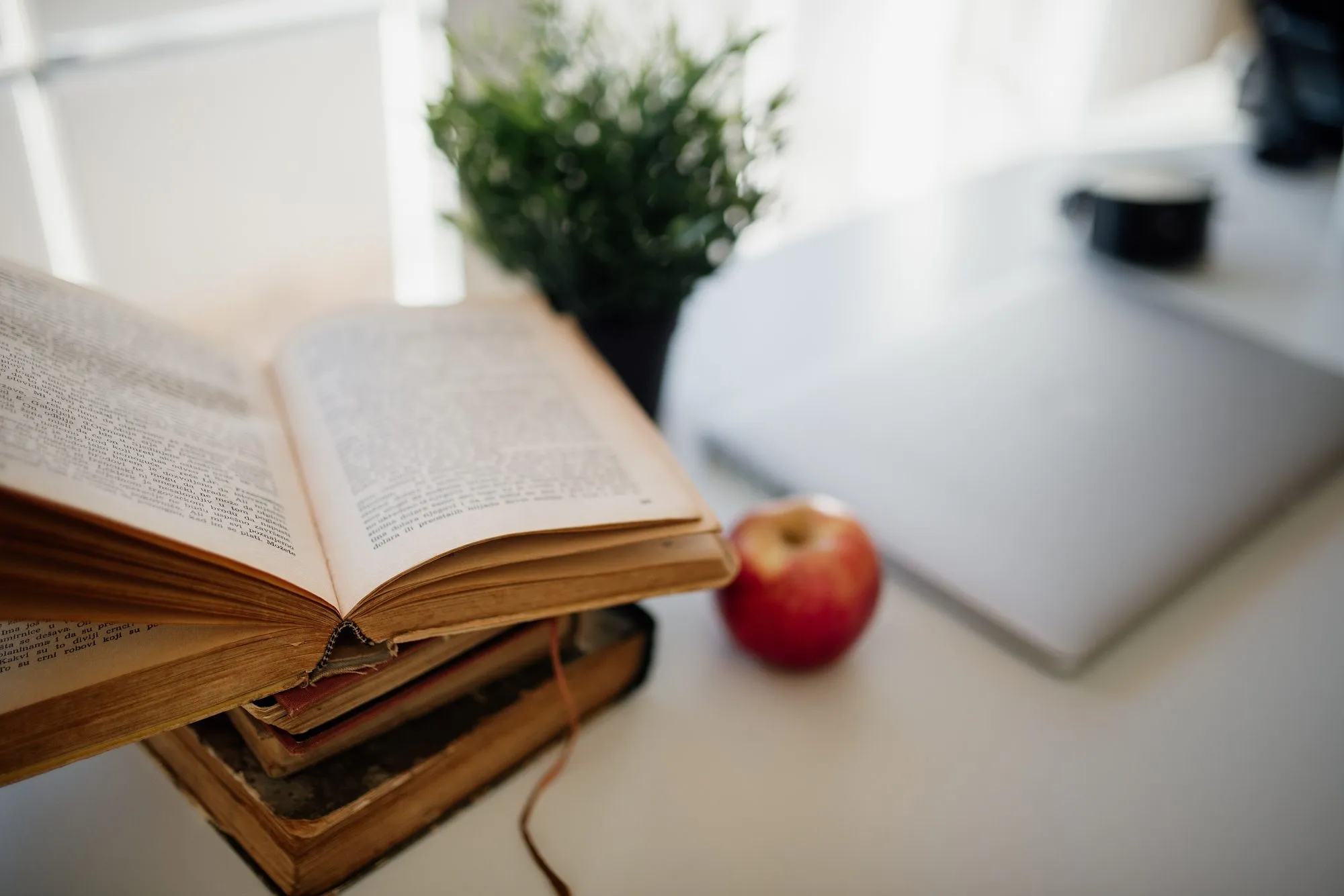 Ein aufgeschlagenes Buch, ein Apfel und ein Laptop auf einem hellen Schreibtisch