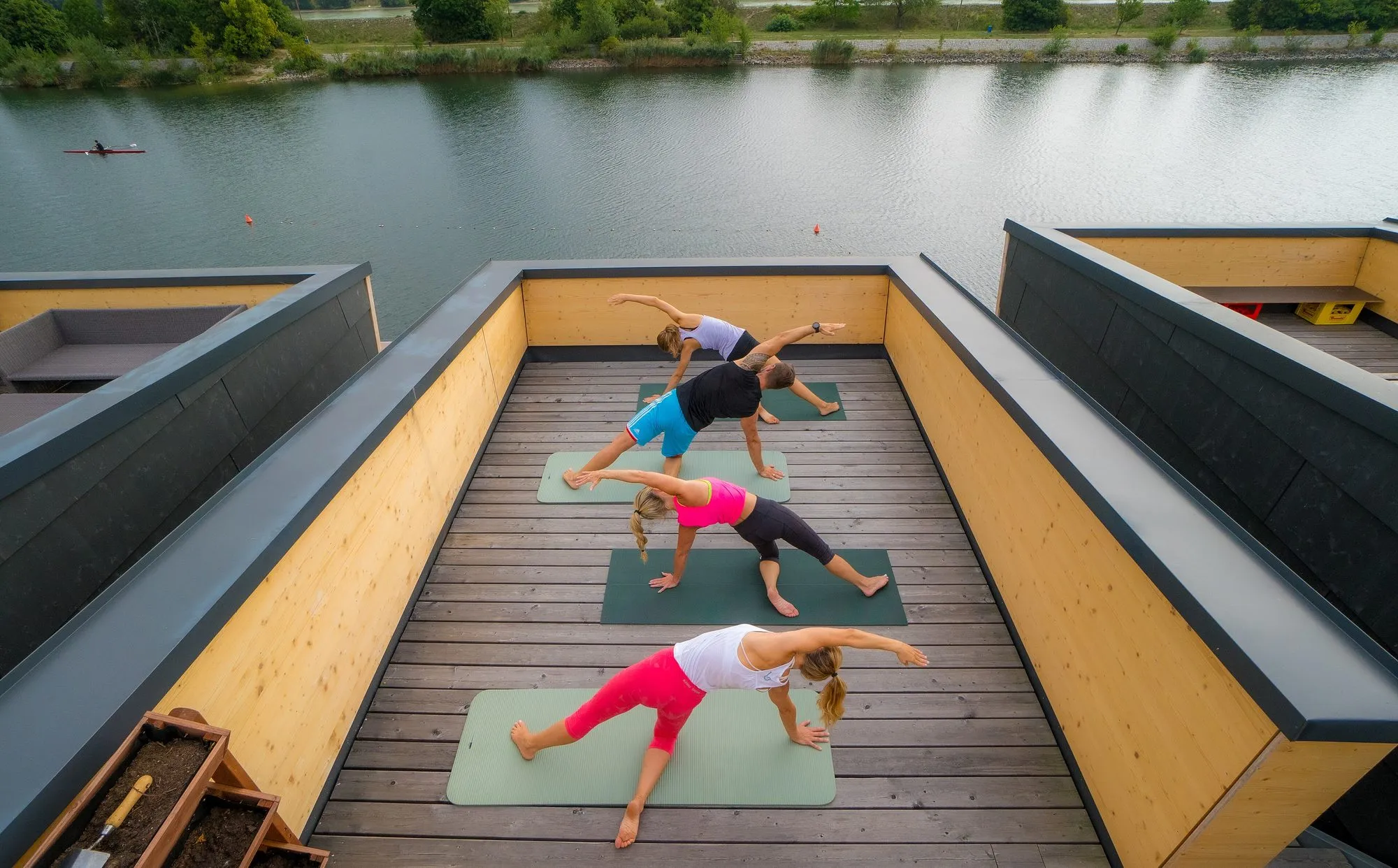 Gruppe beim Pilates auf einer Dachterrasse über dem Wasser, von oben fotografiert