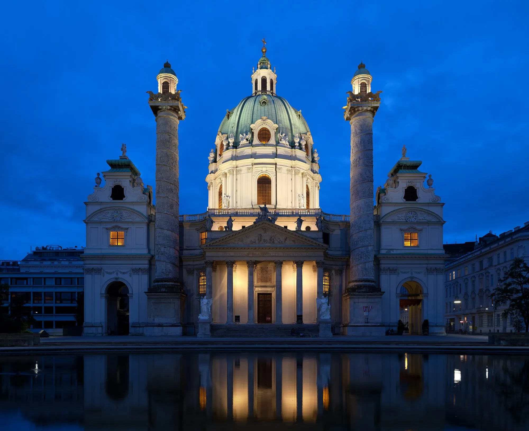 Die beleuchtete Karlskirche in Wien zur blauen Stunde, gespiegelt im Wasserbecken davor